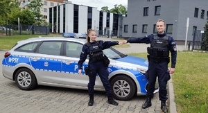 Dwoje umundurowanych policjantów przed radiowozem pozuje do zdjęcia.