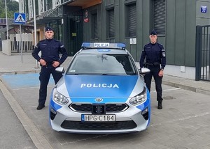 policjanci stoją obok radiowozu.