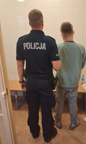 Umundurowany policjant stoi z zatrzymanym mężczyzna - widok z tyłu.