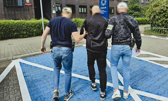 Dwaj funkcjonariusze prowadza zatrzymanego mężczyznę.