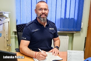 Na zdjęciu umundurowany policjant siedzi przy biurku.