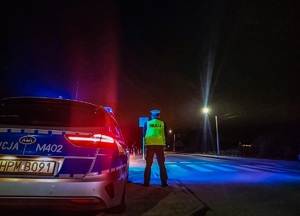 Zdjęcie nocą, policjant przy radiowozie stoi tyłem.