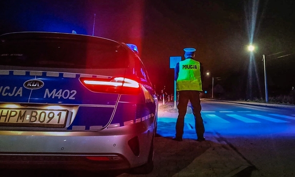 Zdjęcie nocą, policjant przy radiowozie stoi tyłem.