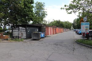 Spalona wiata śmietnikowa, przy garażach i zaparkowane pojazdy.