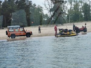 Skuter wodny przy brzegu. Obok quad, samochód terenowy i służby ratunkowe udzielające pomocy poszkodowanemu.