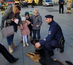 Na zdjęciu umundurowany policjant z psem służbowym, kobieta i dzieci