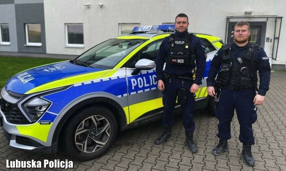 Dwóch umundurowanych policjantów stoi przy radiowozie.