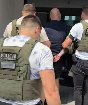 Trzej policjanci w kamizelkach z napisem Policja na plecach prowadzą zatrzymanego.