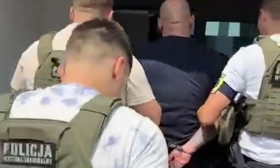 Trzej policjanci w kamizelkach z napisem Policja na plecach prowadzą zatrzymanego.