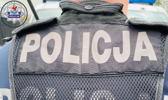 Odwrócony tyłem policjant. Na jego kamizelce znajduje się napis Policja.