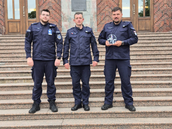 Trzej umundurowani policjanci stoją na schodach i pozują do zdjęcia.