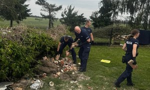 Policjanci sprzątają rozrzucone na posesji cegły po przejściu nawałnicy.