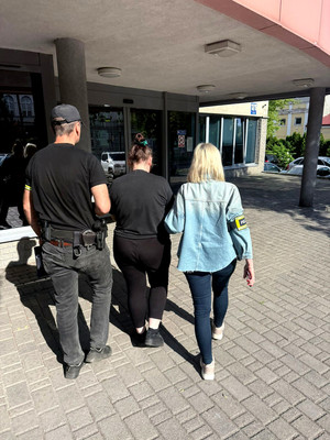 Dwoje nieumundurowanych policjantów prowadzi zatrzymaną kobietę.