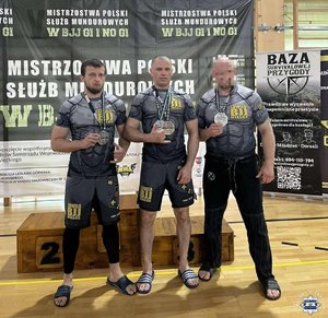 trzech sportowców stoi na podium z pucharem w ręku.