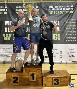 trzech sportowców stoi na podium z pucharem w ręku.