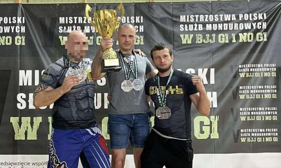 trzech sportowców stoi na podium z pucharem w ręku.