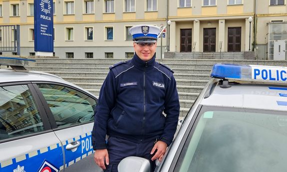 policjant stoi obok dwóch radiowozów.
