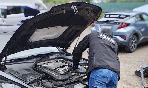 Policjant w kurtce z napisem Policja na plecach, sprawdza auto pod maską.