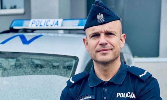 Umundurowany policjant stoi przy radiowozie.
