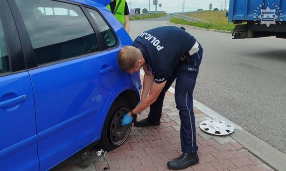 Na zdjęciu policjant w trakcie wymiany koła w pojeździe.