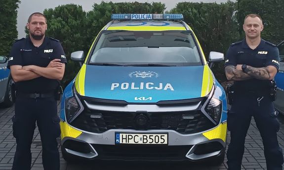 policjanci stoją obok radiowozu.