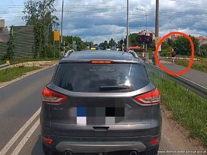 Pieszy przechodzi przez przejazd kolejowy na czerwonym świetle i przy opuszczonych rogatkach.