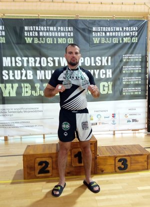 Policjant przy podium trzyma dwa srebrne medale.