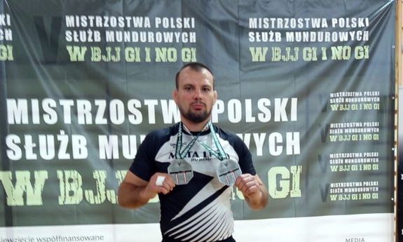 Policjant przy podium trzyma dwa srebrne medale.