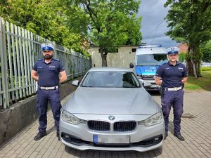 Dwaj umundurowani policjanci przy bmw. Z tyłu widać policyjny radiowóz.