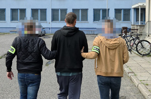 Dwaj nieumundurowani policjanci prowadzą zatrzymanego mężczyznę - widok z tyłu.