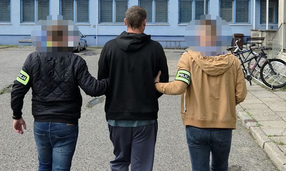 Dwaj nieumundurowani policjanci prowadzą zatrzymanego mężczyznę - widok z tyłu.