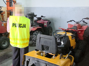 Policjant w żółtej kamizelce z napisem na plecach: Policja, przy zabezpieczonych skradzionych maszynach.