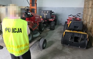 Policjant w żółtej kamizelce z napisem na plecach: Policja, przy zabezpieczonych skradzionych maszynach.