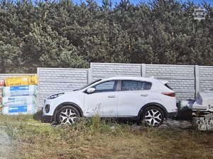 Na zdjęciu stoi biały samochód na podwórzu. W tle materiały budowlane.