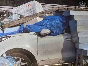 Biały samochód przykryty niebieską plandeką i styropianem.