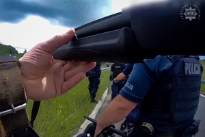 rzut ekranu z kamerki nasobnej - widać trzymana w ręku broń i policjantów.