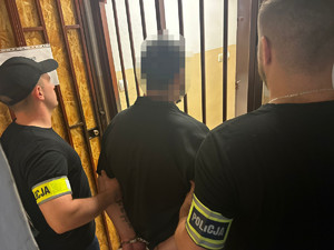 Zatrzymany mężczyzna prowadzony przez dwóch nieumundurowanych policjantów.