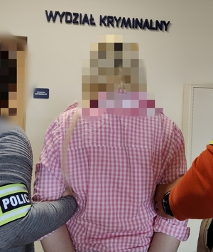 zatrzymana kobieta stoi plecami do aparatu. obok stoi dwóch policjantów.