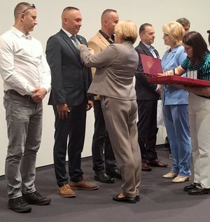 Kobieta przypina mężczyźnie w garniturze odznaczenie.