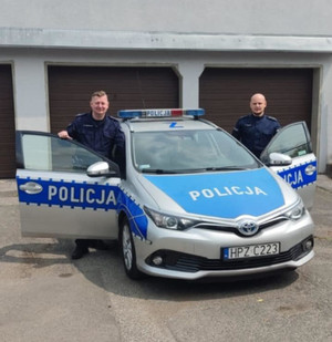 Dwaj umundurowani policjanci w drzwiach radiowozu.