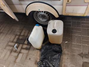 Dwa pojemniki plastikowe z cieczą stoją przy samochodzie.