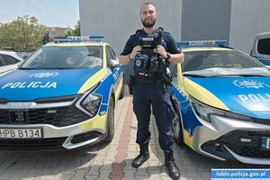 policjant stoi między dwoma radiowozami.