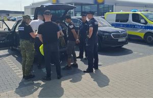 Funkcjonariusze Policji i Straży Granicznej z zatrzymanymi przy aucie.