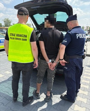 Funkcjonariusze Policji i Straży Granicznej z zatrzymanymi przy aucie.