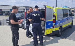 Funkcjonariusze Policji i Straży Granicznej z zatrzymanymi przy policyjnym radiowozie.