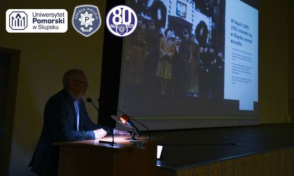 Na zdjęciu mężczyzna, a za nim w tle na ścianie wyświetlana prezentacja multimedialna.