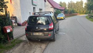 Na zdjęciu ulica, a przy niej zaparkowane dwa samochody i budynki stojące obok drogi