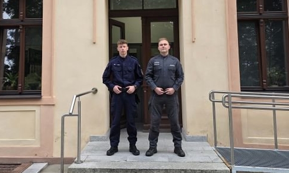 Dwaj funkcjonariusze przed budynkiem komendy Policji.