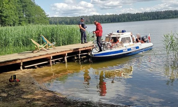 Policyjna łódź dopływa do pomostu. Na pomoście stoi policjant.