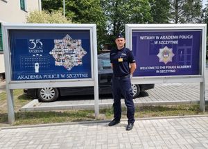 Policjant stoi przy tablicach z napisem Akademia Policji w Szczytnie.